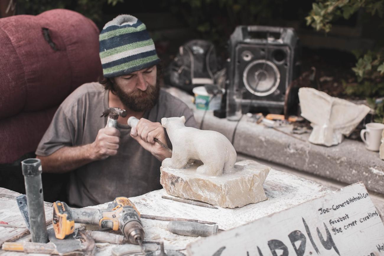 A carver at his bench working a block of white marble, tools laid out around him