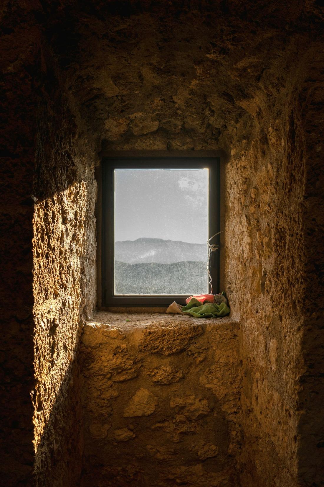 A deep stone window in a Tuscan farmhouse, the valley framed beyond it