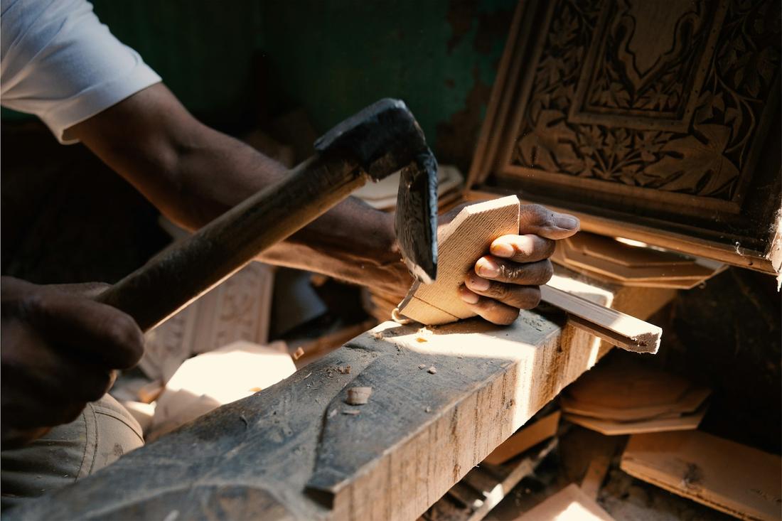 An artisan's hands working a carved wooden panel with a chisel