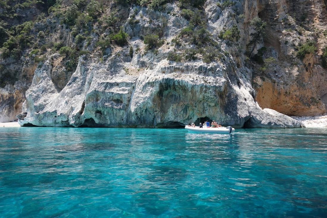 A boat at anchor in clear water below a rock face